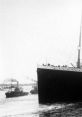 Titanic's iconic bow looms large as smaller tugboats navigate nearby waters, showcasing maritime history and elegance.