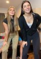 Riley Wagner and a friend pose playfully, showcasing stylish outfits and bright smiles in a casual indoor setting.