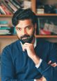 Vimal Dev thoughtful portrait, showcasing his stylish look and engaging expression against a backdrop of books.
