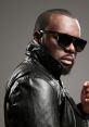 Maître Gims poses confidently in a stylish black leather jacket and sunglasses, showcasing his signature look.