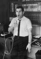 Ross Bagdasarian Jr. passionately performing, holding a microphone in a retro office setting, showcasing his vocal talent.
