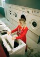 Woman in a red outfit loading laundry into a washing machine at a laundromat, embodying a casual and vibrant atmosphere.