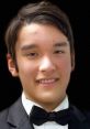 Young male wearing a formal tuxedo and bow tie, smiling against a dark background, showcasing a confident expression.