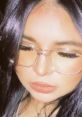 Close-up portrait of a young woman with glasses, featuring soft makeup and stylish, long dark hair.