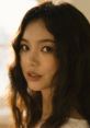 Portrait of a young woman with wavy hair and soft features, radiating natural beauty and elegance in warm lighting.