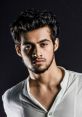 Stylish young man with tousled hair, wearing a white shirt, exuding confidence against a dark background. Keshav's charisma shines.