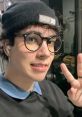 Young person with glasses and a beanie gives a peace sign, enjoying a casual moment in a stylish setting.