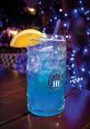Blue cocktail adorned with an orange slice, served in a HB München glass, set against a vibrant, illuminated background.