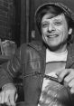 Harlan Ellison smiling while holding a writing tool, showcasing his creative spirit and unique style in a casual setting.