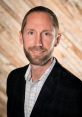 Professional portrait of Brian Kimberlin in a suit, smiling against a textured wooden background.