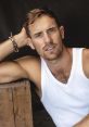 Handsome man with short hair, wearing a white tank top, poses thoughtfully with a wooden background. Actor Joel Jackson.