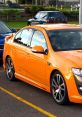 Orange FG Falcon parked in a lot, showcasing sporty design and sleek lines with alloy wheels and a polished finish.