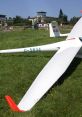 Glider aircraft on grassy field with control tower in the background, showcasing the beauty of aviation and soaring.