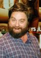 Zach Galifianakis smiles at a promotional event, showcasing his signature beard and casual plaid shirt style.