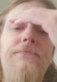 Close-up of a man with a beard, showing a thoughtful expression while resting his forehead with his hand.