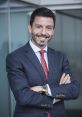 Javier Rosado smiles confidently in a business suit, showcasing professionalism and approachability in a modern office setting.