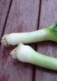 Fresh leeks with green tops and white stems on a wooden surface, showcasing their crisp texture and vibrant color.