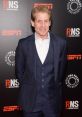 Skip Bayless smiles, dressed in a blue suit, at an ESPN event, showcasing his signature style and charismatic presence.