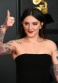 Julia Michaels showcasing her stylish look at a Grammy event, confidently giving a thumbs up and displaying her tattoos.
