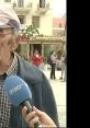 Elderly man being interviewed in a public square, with people in the background engaging in conversation and activities.