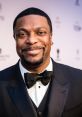 Chris Tucker smiling in a black tuxedo with a bow tie, exuding charm at a red carpet event. Iconic comedian and actor.