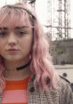 Young woman with pink wavy hair wearing a striped shirt and checkered jacket, set against a city backdrop.