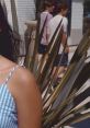 Young woman in a striped dress stands in focus, with two people strolling in the background, highlighting summer vibes.