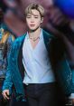JiMin from BTS performing on stage, wearing a stunning turquoise outfit, captivating the audience with his presence.
