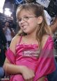 Cheerful child in a pink dress, smiling at a media event, capturing the joy of youth and celebration.