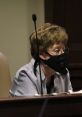 Woman speaking at a meeting, wearing a black mask and striped shirt, focused on the discussion.